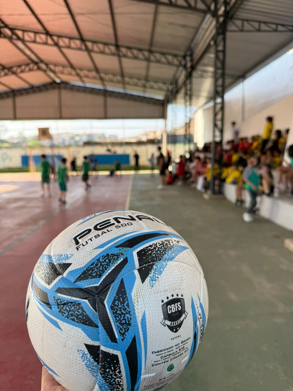 Bola de futsal em primeiro plano na quadra coberta do colégio